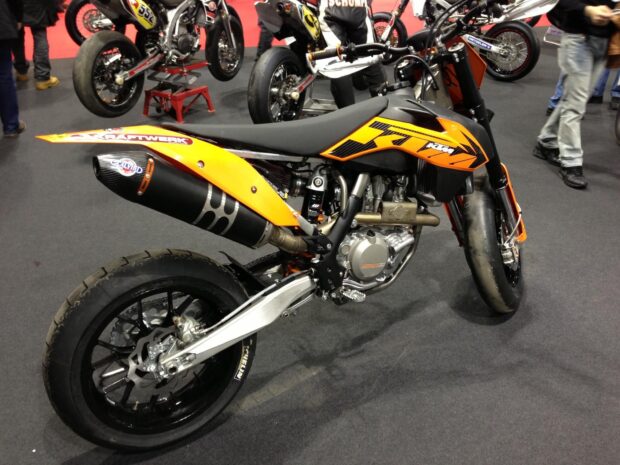 A detailed supermoto bike with orange and black colors displayed at a motorcycle expo