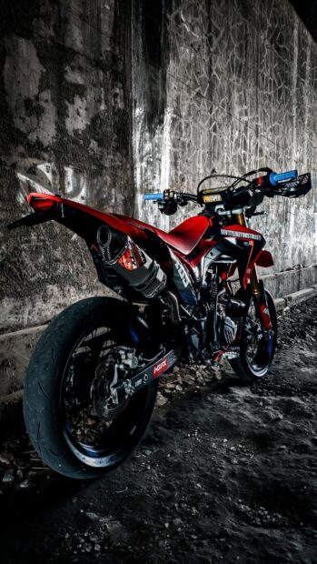 Red supermoto bike parked near a textured wall in an urban setting