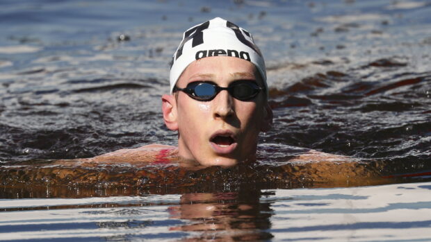 A swimmer wearing a white cap and black goggles swimming in dark water