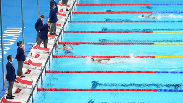 Competitive swimming race with swimmers in lanes and judges standing by the pool