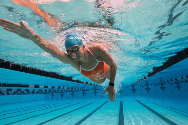 A swimmer wearing a swim cap and goggles swimming freestyle in a pool lane