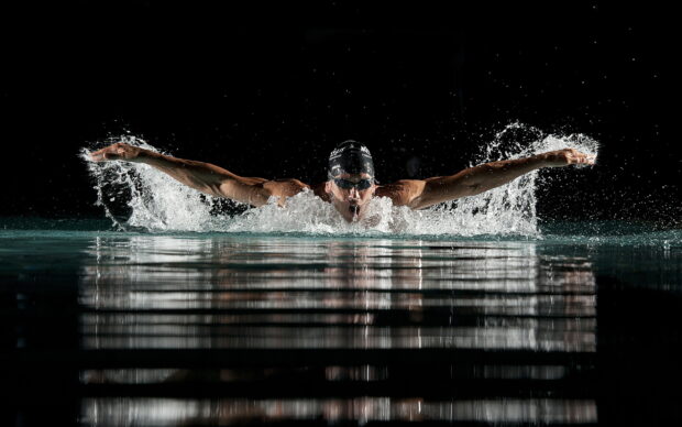 A swimmer performing butterfly stroke with splashing water in a dark pool