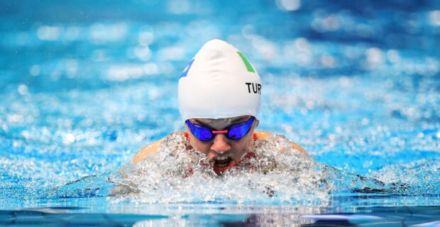 A swimmer wearing a swim cap and goggles powering through water with splashes around during swimming