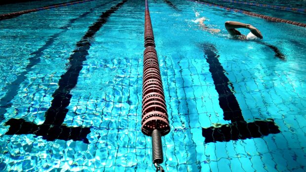 A swimmer practicing swimming in a clear blue pool lane with floating dividers