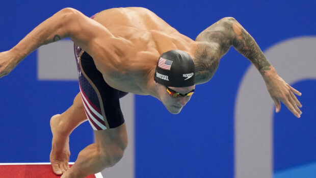 Male swimmer with tattoos diving into the pool to start a swimming race