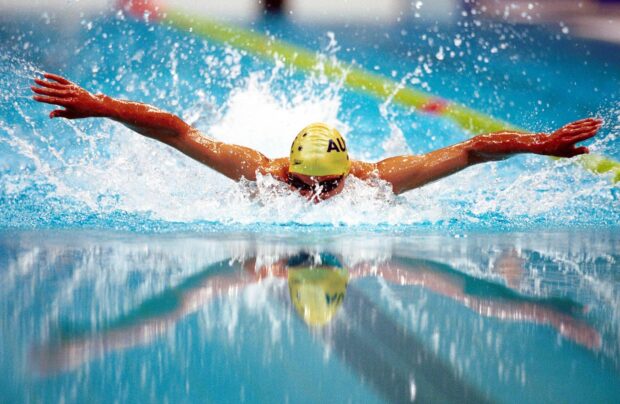A professional swimmer performing butterfly stroke in a clear blue pool
