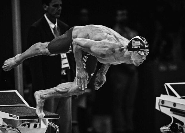 A swimmer diving from the starting block showing strength and swimming skills
