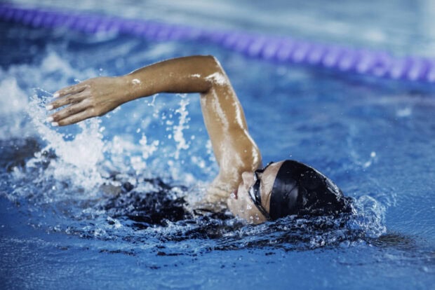 A swimmer performing freestyle stroke in a blue pool with clear water and splashes