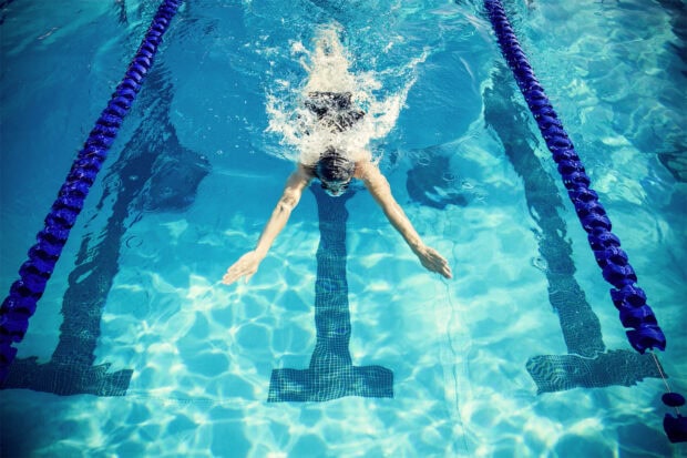 A swimmer swimming in a pool performing a butterfly stroke with clear blue water and lane dividers