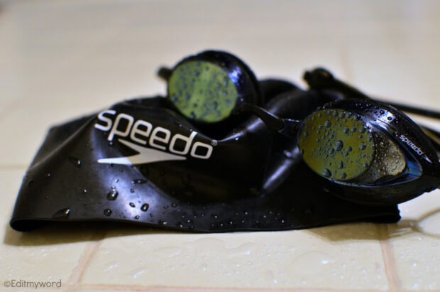 Swimming goggles and cap with water drops on a tiled surface showing swimming gear