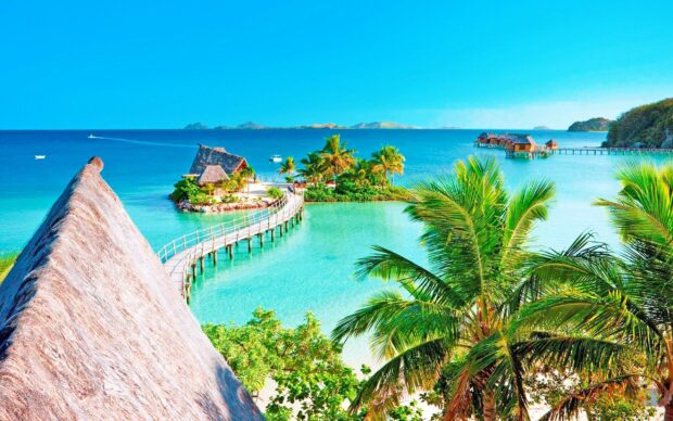A tropical island with palm trees and a wooden walkway in Tahiti surrounded by clear turquoise water