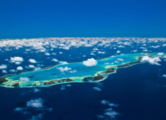 Aerial view of Tahiti island and surrounding turquoise waters under a bright blue sky with scattered clouds