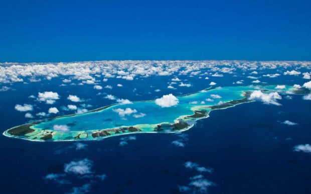 Aerial view of Tahiti island and surrounding turquoise waters under a bright blue sky with scattered clouds