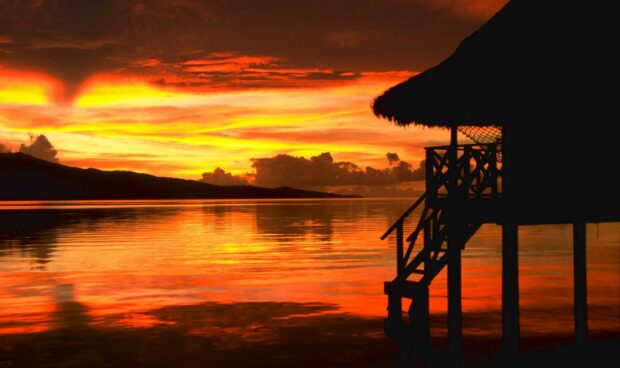 Tropical sunset over water with tahiti hut silhouette and vibrant orange sky