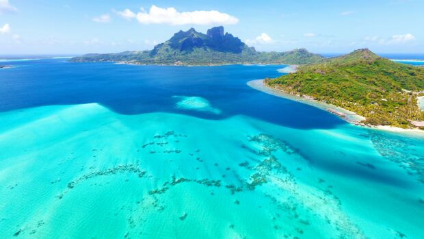 Aerial view of Tahiti island with turquoise water and lush green mountains under blue sky