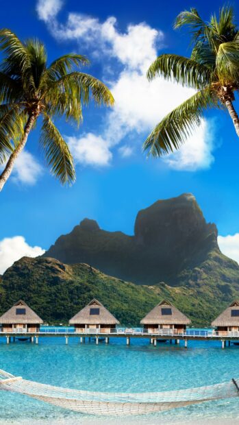 Tropical paradise in Tahiti with overwater bungalows and palm trees against a clear blue sky