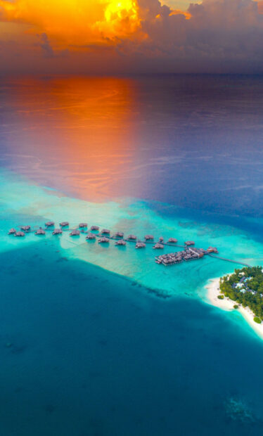 Sunset over clear turquoise waters in Tahiti with overwater bungalows and tropical island