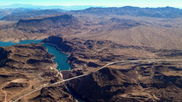 Aerial view of the Colorado River flowing through a rocky canyon landscape with a large dam and bridge