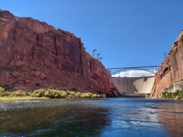 Red rock cliffs surround the Colorado River near a large dam structure