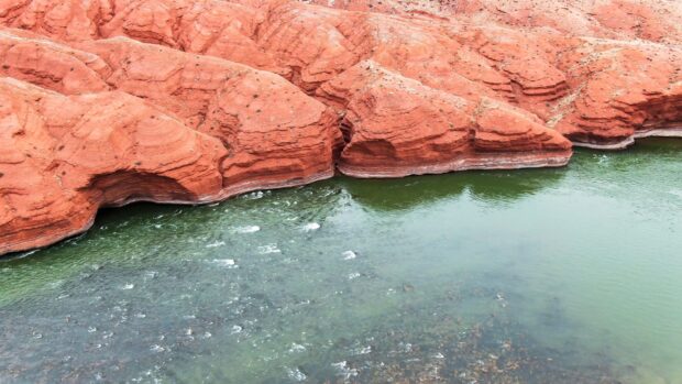 Red rock formations along the Colorado River with clear green water and natural erosion patterns