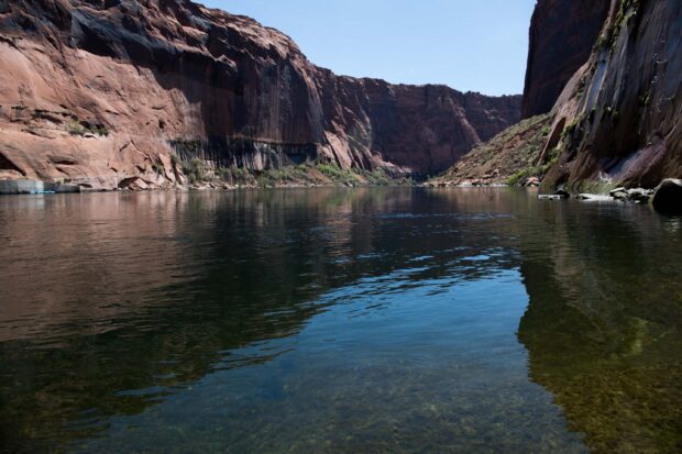 Rocky canyon walls reflecting in the clear waters of the Colorado River under a bright blue sky