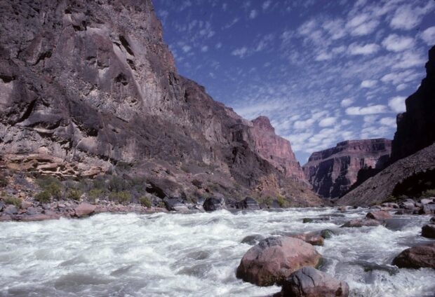The Colorado River flowing rapidly through the rocky canyon under a cloudy sky