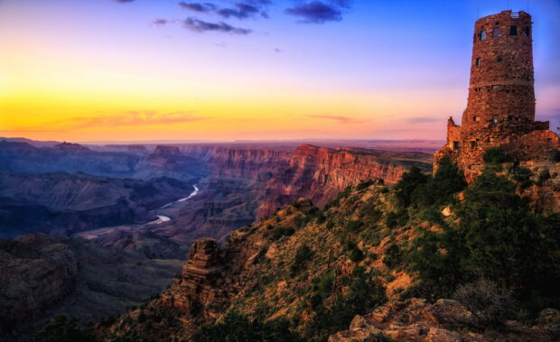 The Colorado River winding through the Grand Canyon at sunset with a stone tower on the cliff