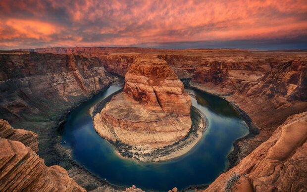 A natural rock formation surrounded by the Colorado River winding through the desert canyon at sunset