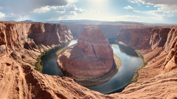 The Colorado River winding through the canyon with surrounding red rock cliffs in bright sunlight