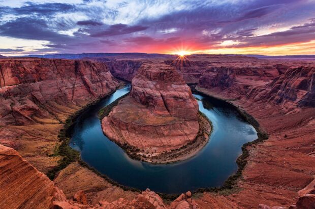 The Colorado River winding through red rock canyons at sunset with vibrant sky colors
