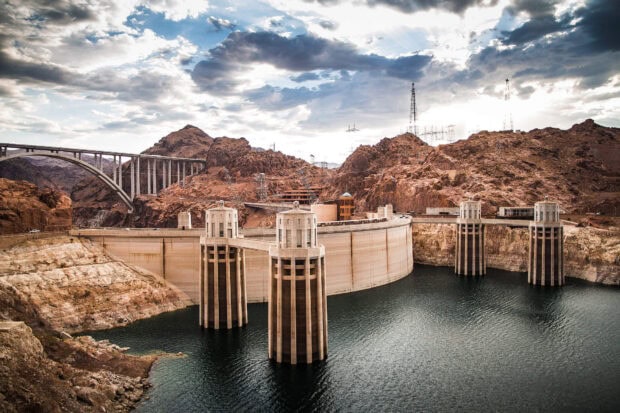 The Hoover Dam structure on the Colorado River with surrounding desert mountains and cloudy sky