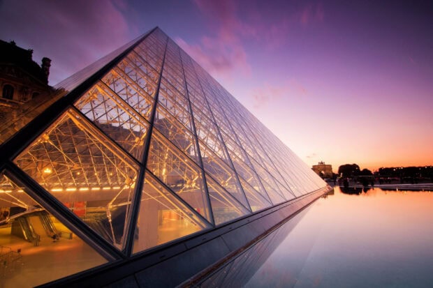 The Louvre glass pyramid illuminated at sunset reflecting the sky and surroundings