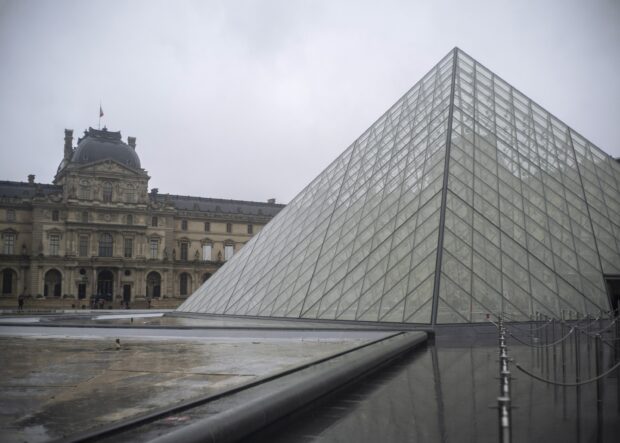 The Louvre museum with its iconic glass pyramid on a cloudy day