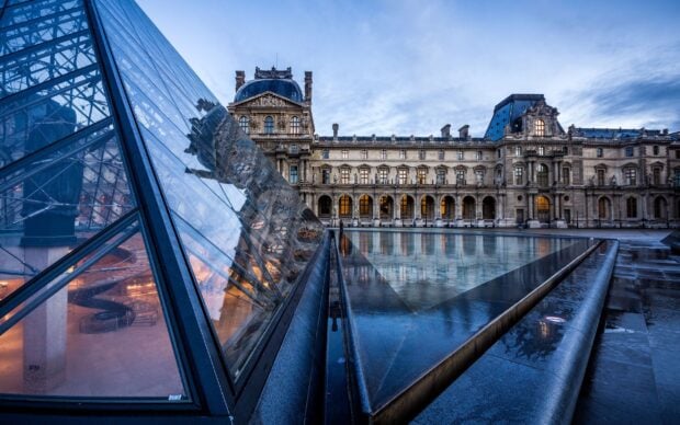 The Louvre reflecting on glass pyramid in Paris during evening blue hour