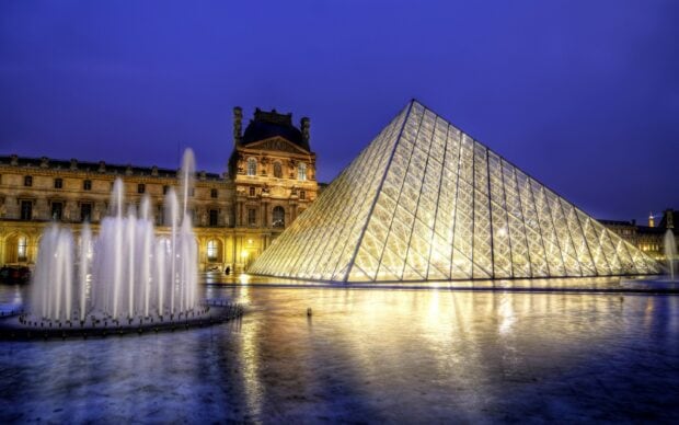 The Louvre building with the glass pyramid illuminated at night