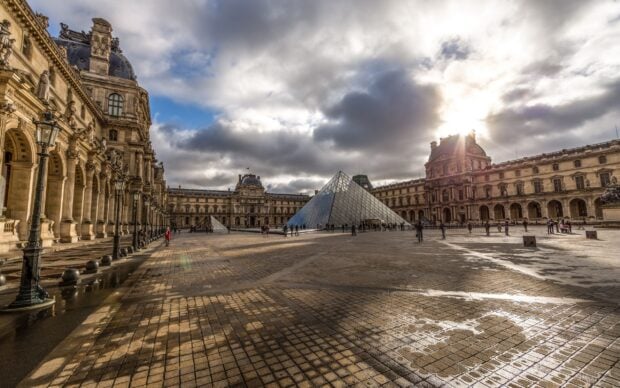 The Louvre courtyard with glass pyramid and historic museum building under cloudy sky