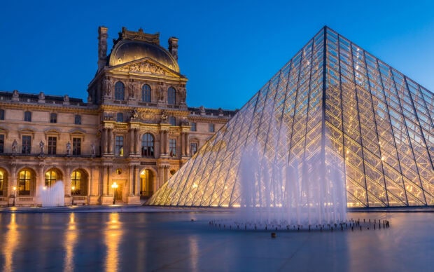 The Louvre architectural detail with illuminated glass pyramid and fountain at dusk