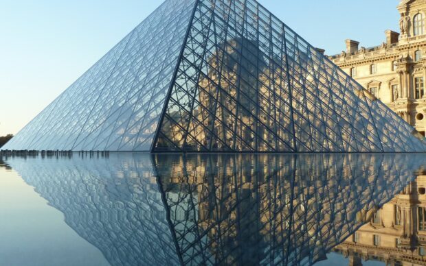 The Louvre glass pyramid reflecting on the water during sunset in Paris France