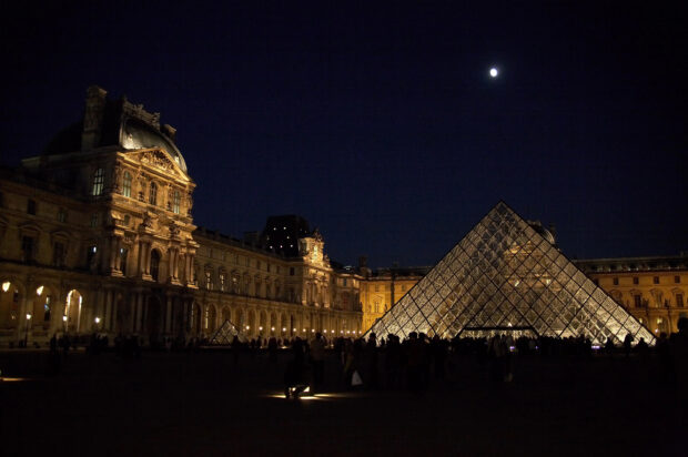 The Louvre museum and glass pyramid illuminated at night under the moonlight
