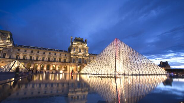 The illuminated glass pyramid and Louvre Museum building at dusk in Paris