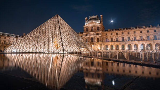The Louvre glass pyramid and historic museum building reflecting on water at night
