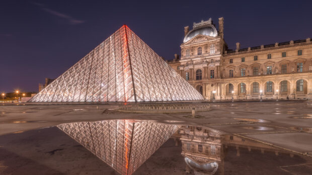 The Louvre glass pyramid and historic palace reflected on wet ground at night