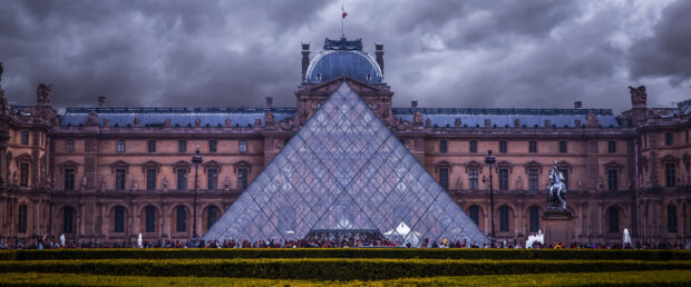 The Louvre glass pyramid with historic palace under cloudy sky