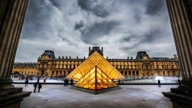 The Louvre museum with glass pyramids under cloudy sky in Paris