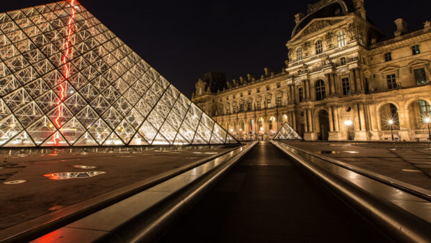 Illuminated glass pyramid and historic architecture at night in Paris