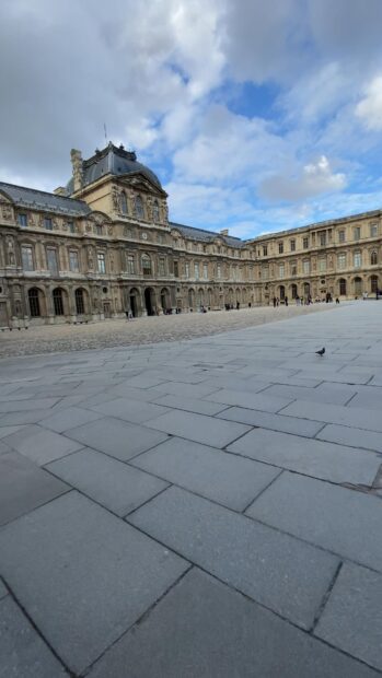 The Louvre architecture and courtyard under a cloudy sky with people walking