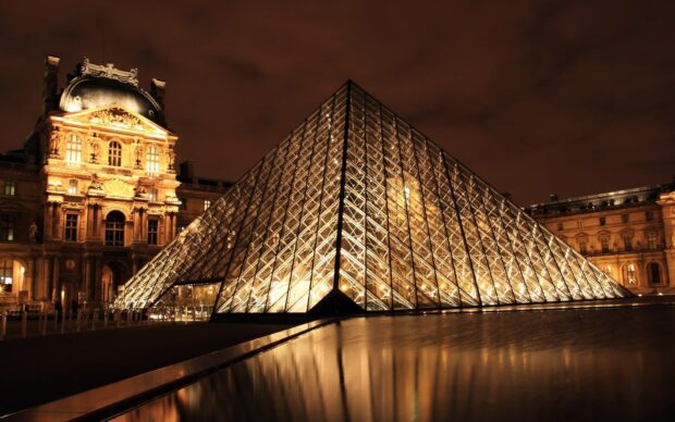 The Louvre pyramid illuminated at night with historic architecture reflected on water