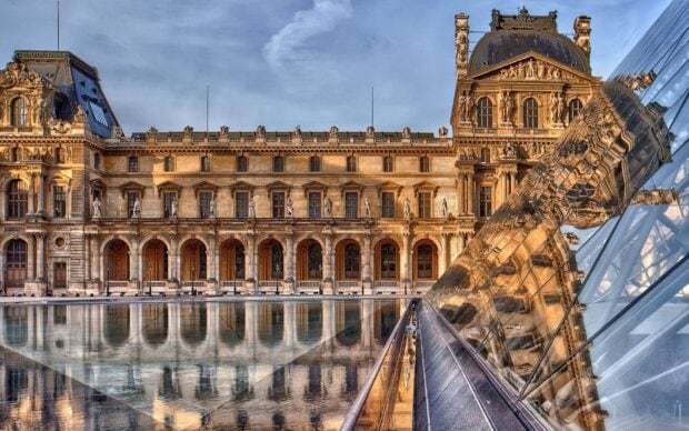 Historic Louvre architecture reflected in the glass pyramid at sunset
