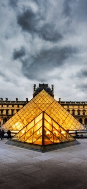 Illuminated glass pyramid at the Louvre under cloudy skies in Paris