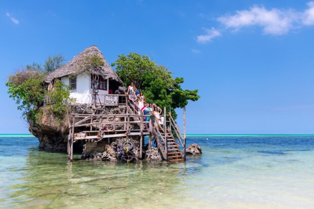 A group of people stands on the wooden stairs of The Rock Restaurant surrounded by clear ocean water, HD Desktop Wallpaper